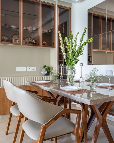 Dining table with marble top and wooden X-leg base beneath glass-front copper-framed cabinets