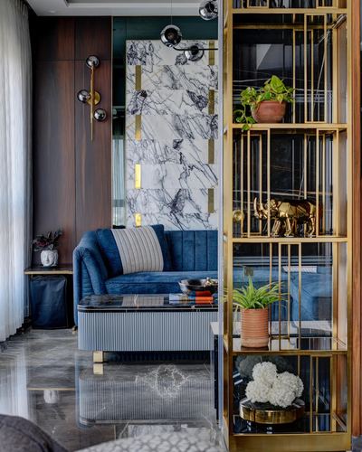 Living room with blue velvet sofa, marble feature wall, and gold-framed glass shelving unit in foreground