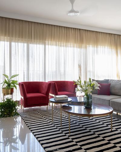 Living room with red velvet chairs, striped rug, and round brass coffee tables by sheer curtains