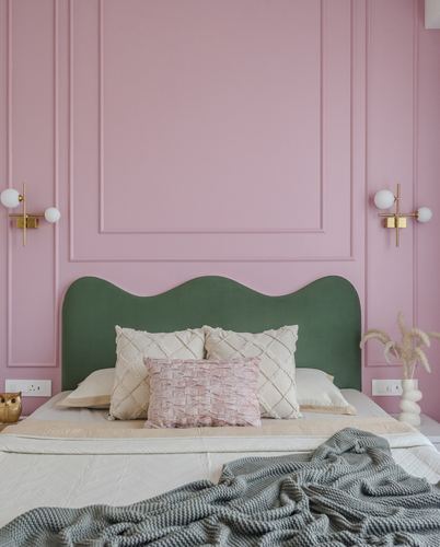 Pink paneled bedroom wall with green scalloped headboard, brass sconces, and layered pillows