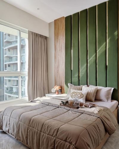 Bedroom with green fluted velvet headboard wall, brass lights, and beige bedding beside a window