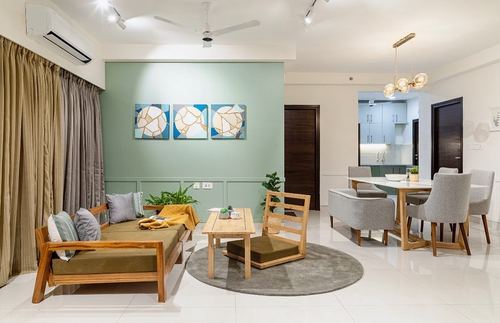Living room with sage wall, wooden sofa, round rug, and dining area beyond