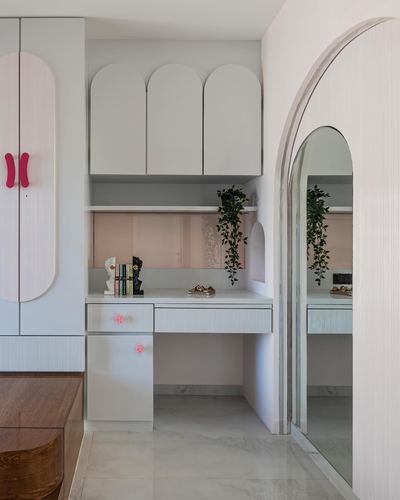 White dressing nook with arched cabinet doors, mirror, and pink accents