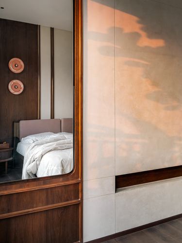 Arched mirror reflecting a bedroom beside a textured plaster wall with warm light
