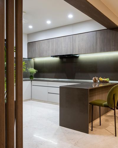 Modern kitchen with dark backsplash, wood cabinetry, stone floor, and olive chair at island.