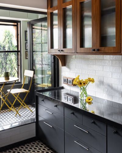 Kitchen corner with wood cabinets, black counters, subway tile, and a small balcony seating nook