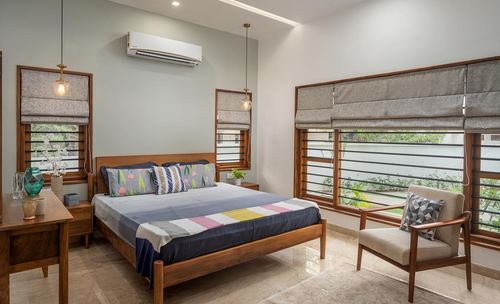 Bedroom with wooden bed, patterned pillows, hanging pendant lights and slatted windows overlooking greenery