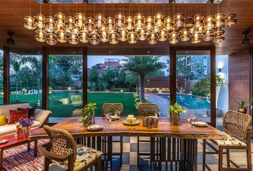 Sunroom dining area with cluster pendant lights, live-edge table, cane chairs, opening to garden and pool