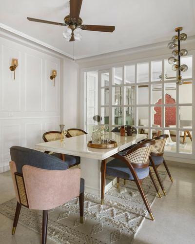 Dining room with marble table, cane chairs, brass sconces and glass partition to adjoining room