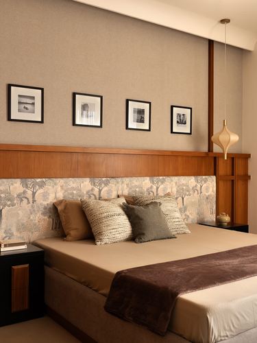 Bedroom with wood-trimmed headboard wall, patterned fabric panel, layered cushions, and framed photos above