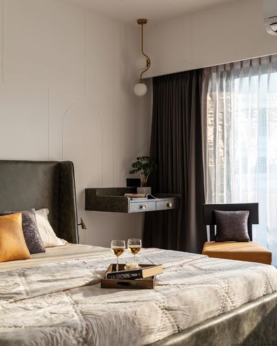 Bedroom with olive leather headboard, floating nightstand, arched wall panelling, and dark curtains by window.