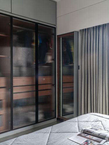 Bedroom corner with fluted glass wardrobe doors, grey curtain, and quilted bed with magazine.