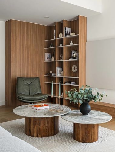 Living room corner with wood shelving, green leather chair, and round marble-top coffee tables