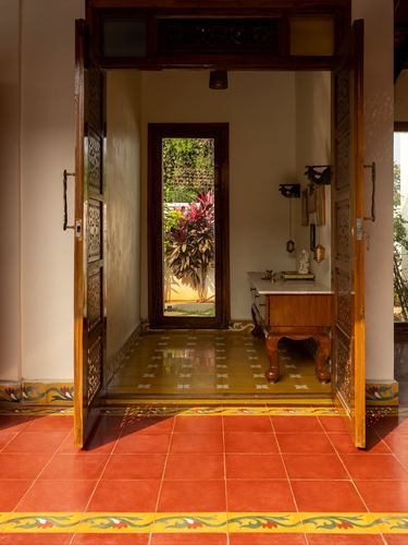 Carved wooden doors open onto a patterned tile foyer leading to a garden-facing door beyond