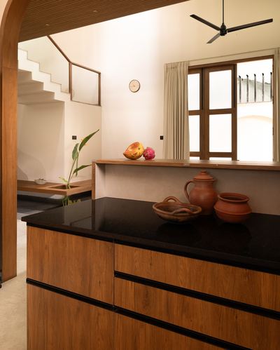 Wooden kitchen island with black countertop, terracotta pots, window and staircase beyond
