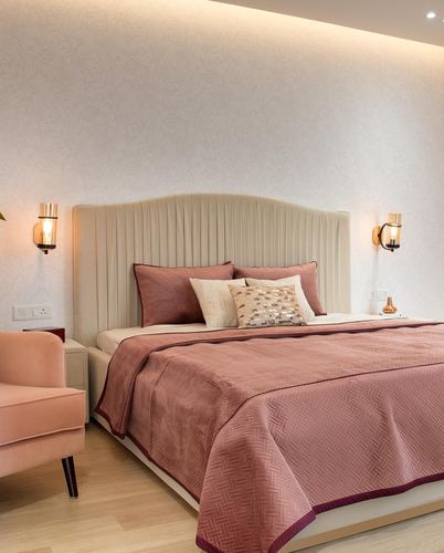 Bedroom with pleated cream headboard, dusty rose bedding, and warm sconces on textured wall