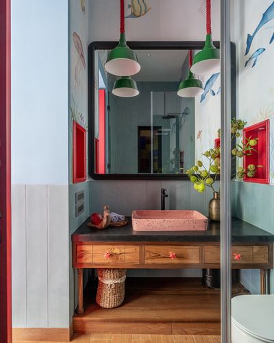 Bathroom vanity with pink terrazzo-look sink, green pendant lights, teal marine wallpaper, wooden drawers with star pulls.