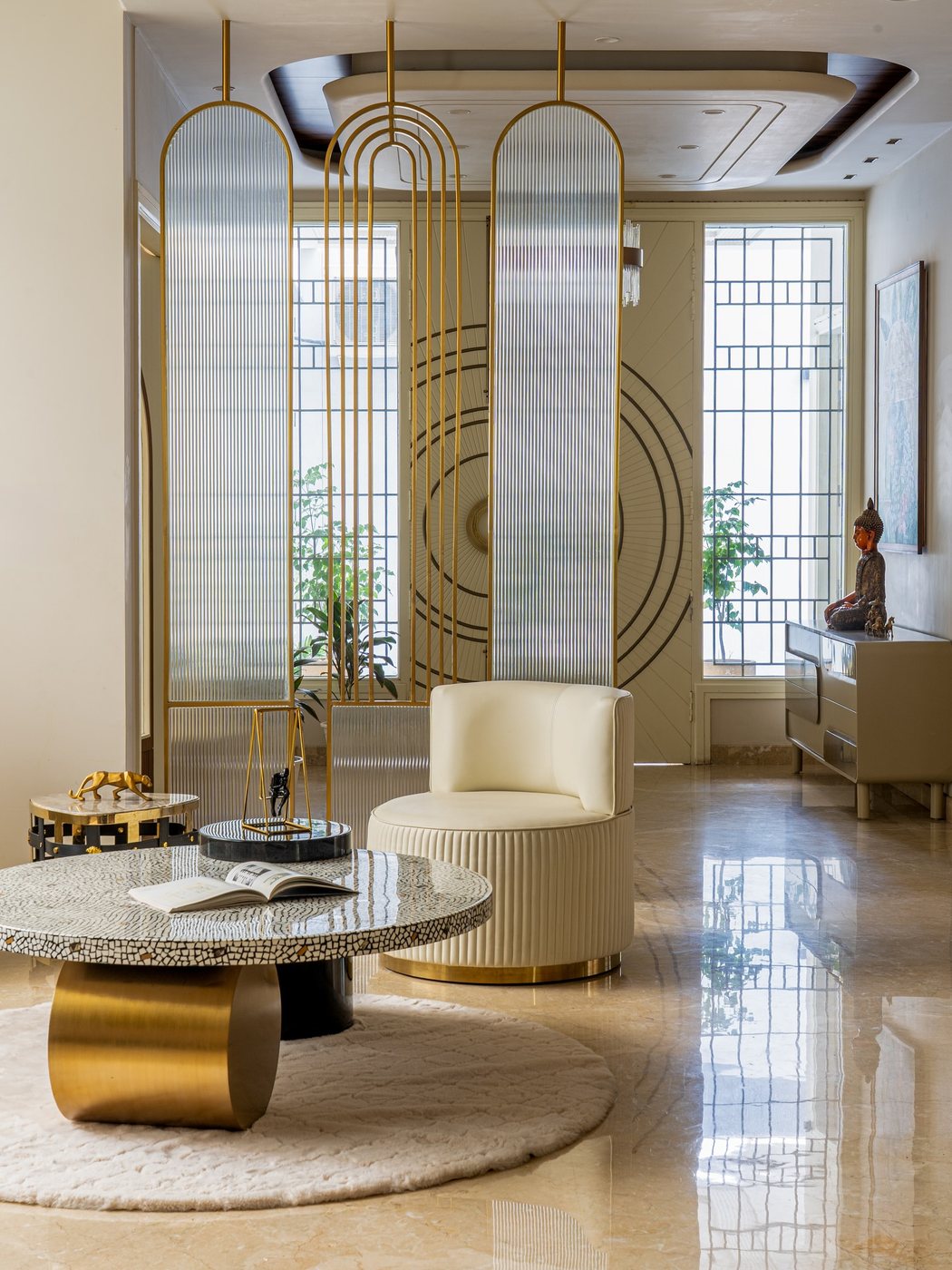 Foyer with arched fluted glass screens, round inlaid coffee table, and cream bolster chair on marble floor