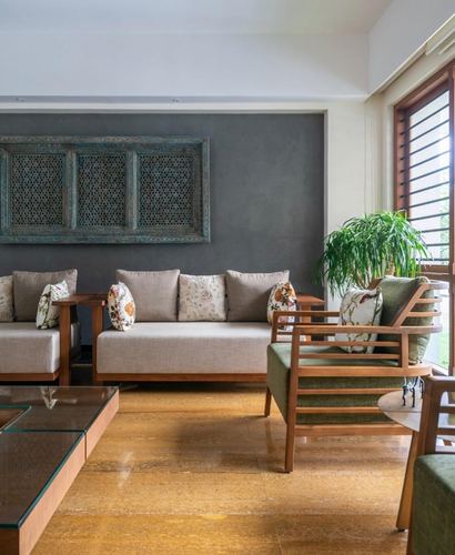 Living room with beige sofas, green armchair, carved wooden panel on grey wall, stone floor