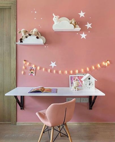 Pink-walled kids study nook with floating white desk, pink chair, and cloud shelves with plush toys