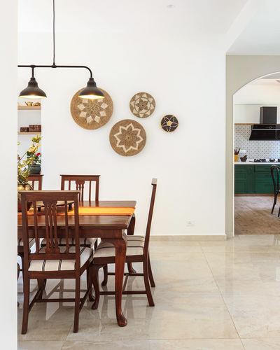 Dining room with wooden table and chairs, woven wall plates, view into green kitchen beyond