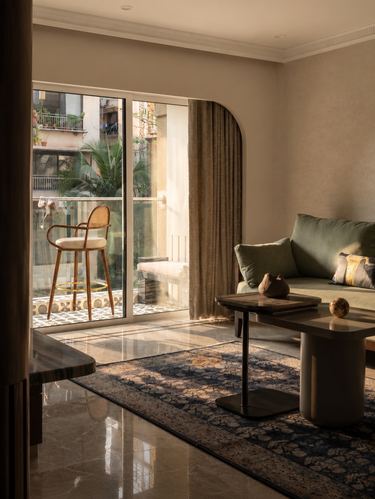 Living room with arched curtained doorway, cane bar stool, olive sofa, and dark coffee table on patterned rug