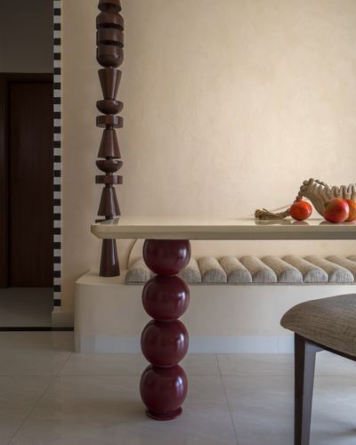 Close-up of a stacked maroon sphere table leg beside a scalloped bench and turned wood pillar