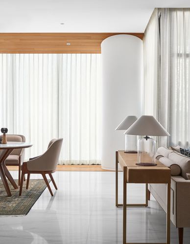 Living and dining space with sheer curtains, a curved white column, marble floor and a wooden console table