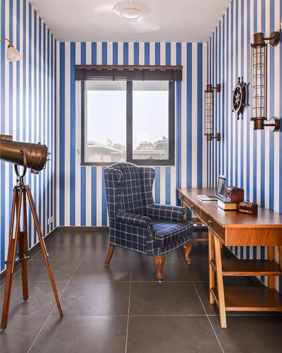 Nautical-themed study nook with blue striped walls, plaid wingback chair, wooden desk and vintage telescope