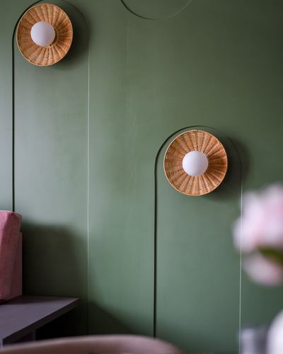 Two round cane wall sconces on arched metal frames against a sage green wall