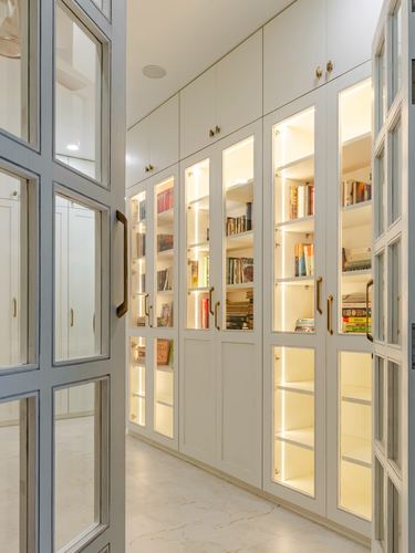 Corridor lined with white glass-front bookcases lit from within, glass door in foreground