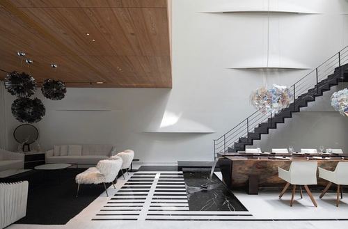 Double-height living and dining space with wooden ceiling, black staircase and sculptural pendant lights