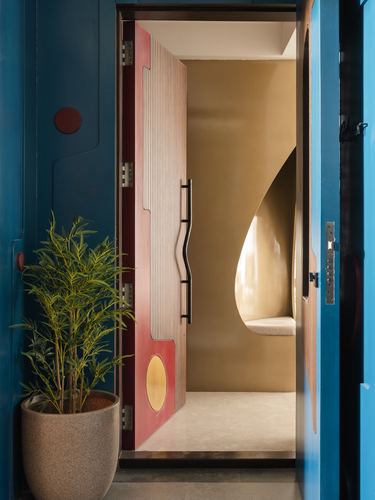 Fluted red door with brass circle opens to a curved mustard alcove entryway