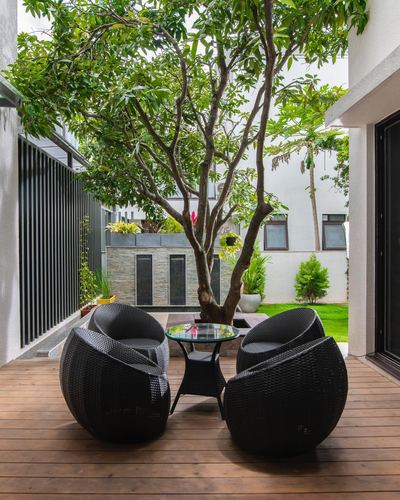 Wooden deck with black wicker chairs facing a courtyard tree and stone wall