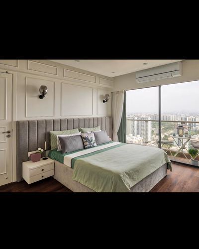 Bedroom with grey channel-tufted headboard, green bedding, and floor-to-ceiling city view windows