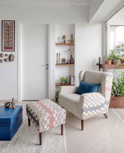 Wingback armchair and patterned ottoman beside a shelved niche and balcony view