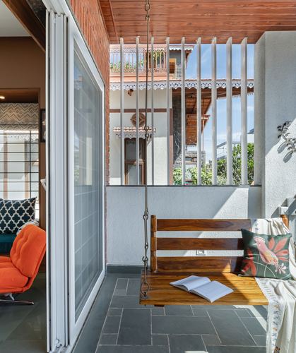 Wooden hanging swing on a stone-floored balcony framed by a vertical metal grille and terracotta rooftop view
