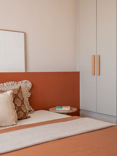 Bedroom corner with terracotta headboard wall, wardrobe with wooden handles, and patterned cushions