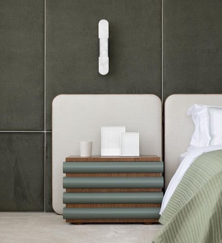 Nightstand with ribbed green drawers beside upholstered bed headboard and marble sconce