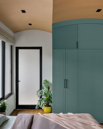 Bedroom corner with teal wardrobe, arched wood ceiling, frosted door, and a potted monstera plant