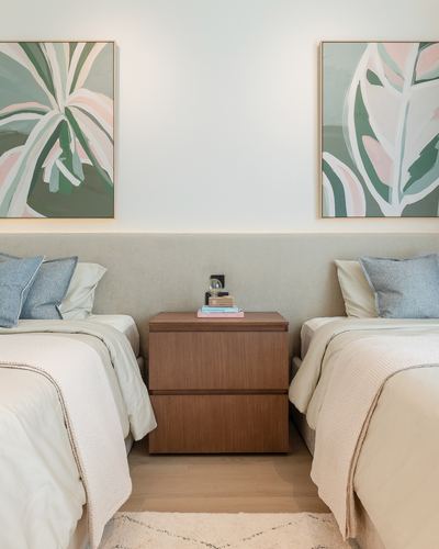 Symmetrical twin bedroom with upholstered headboards, wood nightstand, and botanical artwork above each bed