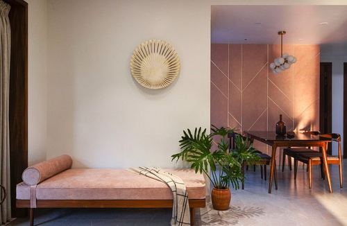 Blush velvet daybed below a sunburst wall sculpture, with dining area and pendant light beyond.