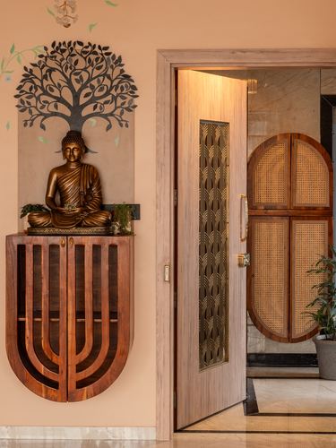 Entryway with carved wooden console, bronze Buddha statue, and open door showing cane-paneled interior