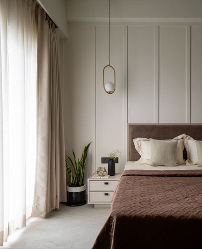 Bedroom corner with panelled wall, brass pendant light, upholstered brown headboard and sheer curtains