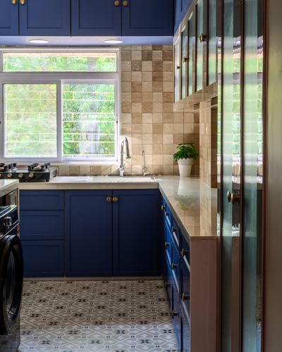 Navy blue L-shaped kitchen with beige tile backsplash, patterned floor and window with greenery view