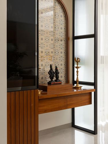 Wooden console table with brass diya lamps beneath an arched patterned tile niche framed in black metal