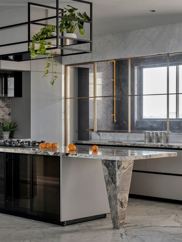 Grey marble kitchen island with waterfall leg, brass-framed window, hanging plant rack overhead