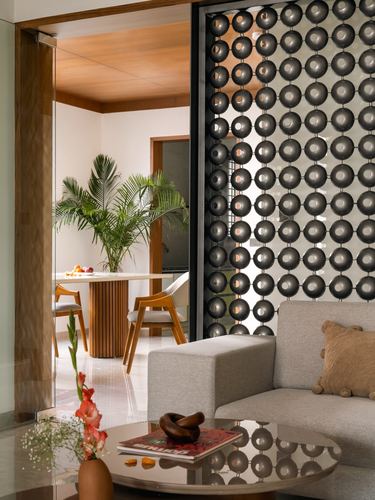 Living room with grey sofa beside a bubble-textured metal screen divider, dining area beyond