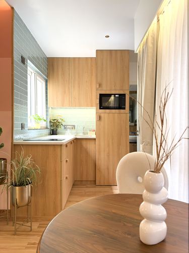Wooden L-shaped kitchen with blue tile backsplash, seen past a dining table with sculptural vase