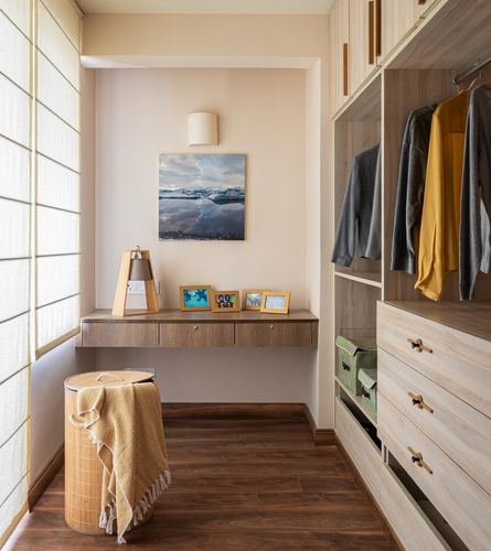 Floating wood desk in a niche beside an open wardrobe with hanging clothes